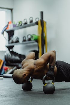 Fit man engages in intense push-up exercise using kettlebells inside gym.