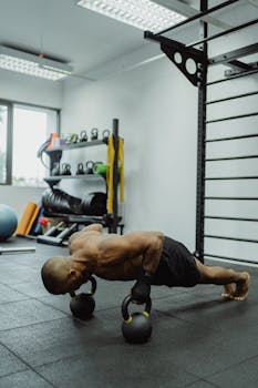 Athletic man doing push-ups on kettlebells in a modern gym setting.