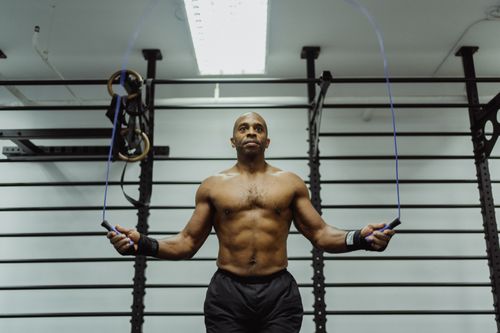 Free Fit man jumping rope shirtless in a gym setting, showcasing fitness and strength. Stock Photo