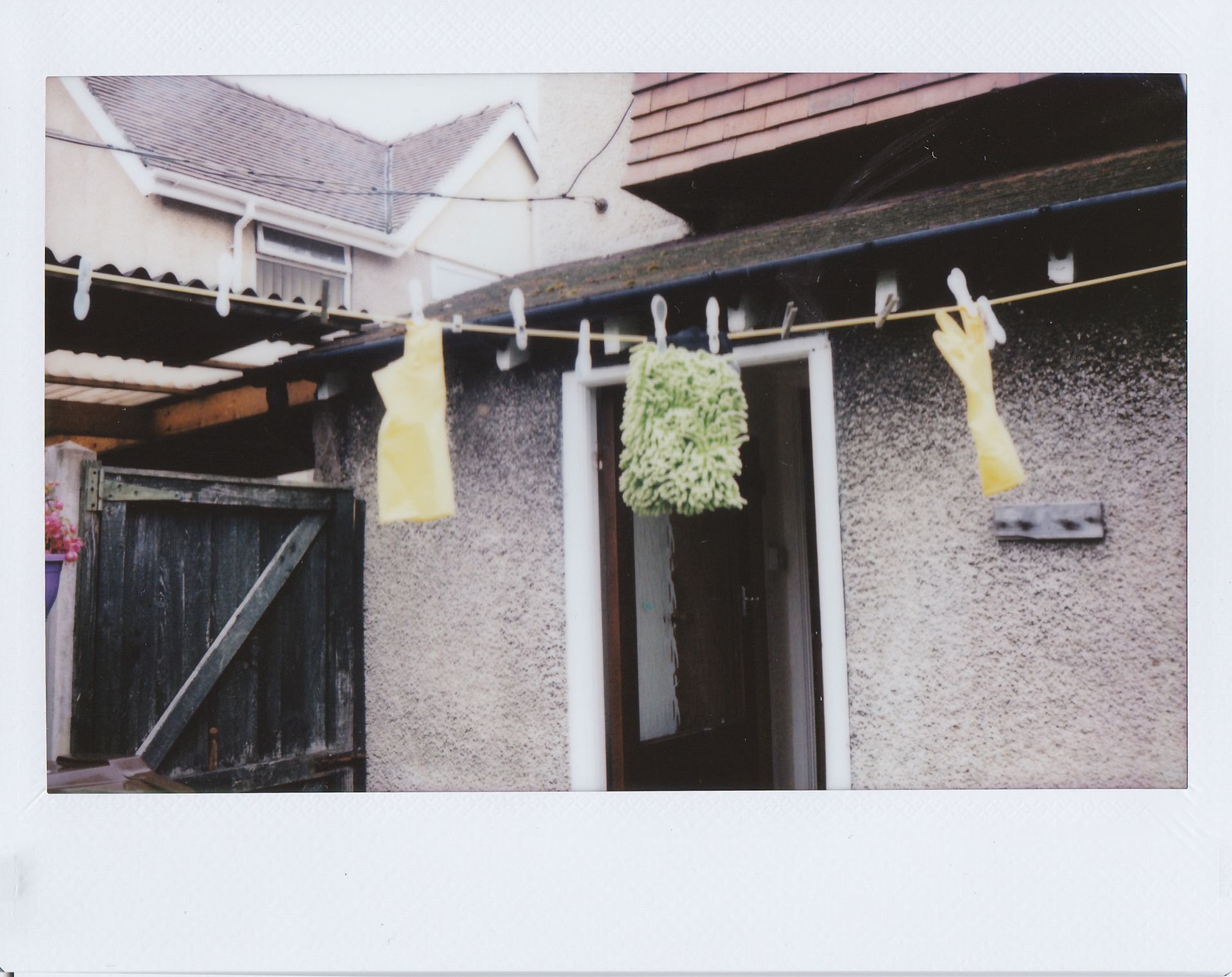 Outdoor house scene featuring laundry with yellow rubber gloves and a green mop head drying.