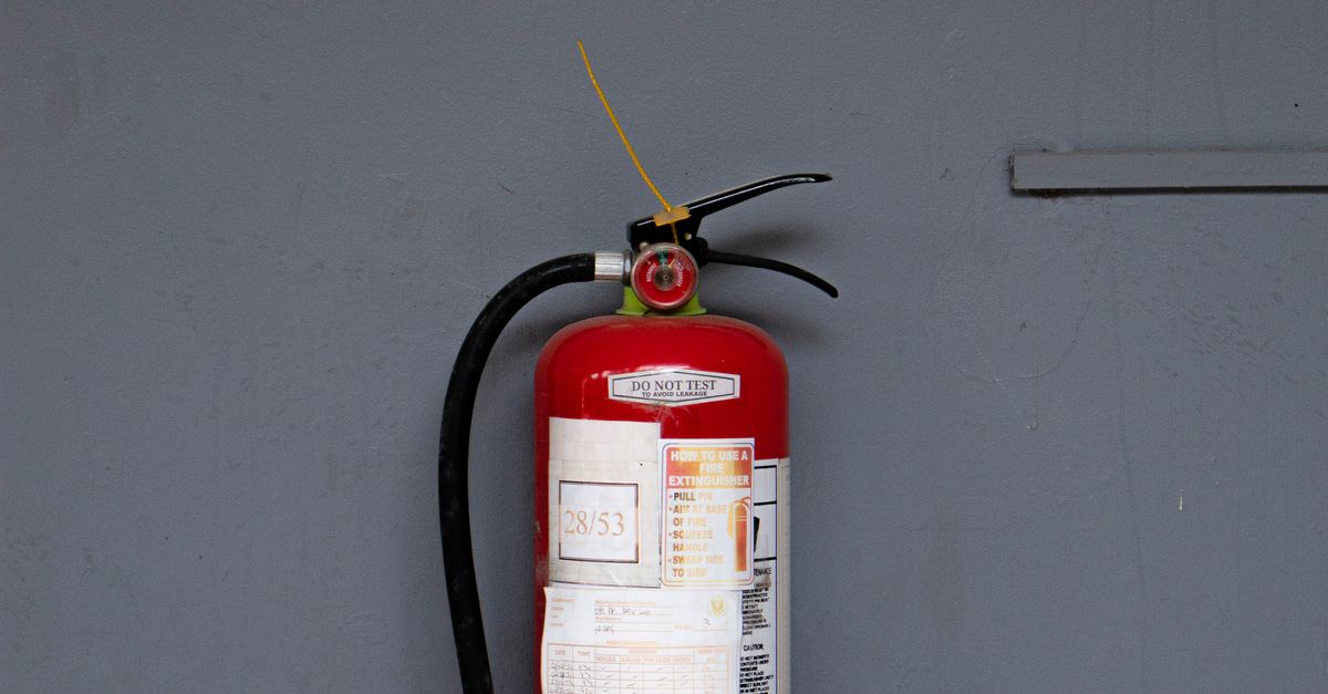 Photo by Nothing Ahead Red fire extinguisher positioned against a gray wall showing safety equipment