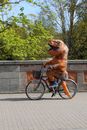 Amusing faceless person in dinosaur costume cycling on sidewalk