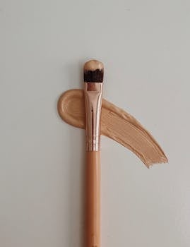 Artistic flat lay of a makeup brush with foundation on a beige background, emphasizing beauty and style.