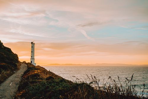 Free Beacon on mount with narrow path near rippled sea under bright cloudy sky at sunset Stock Photo