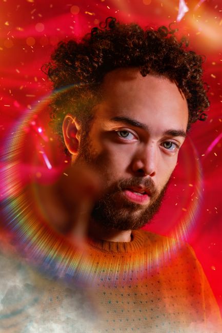 Young bearded confident male with curly hair against red and shining colorful flash around head