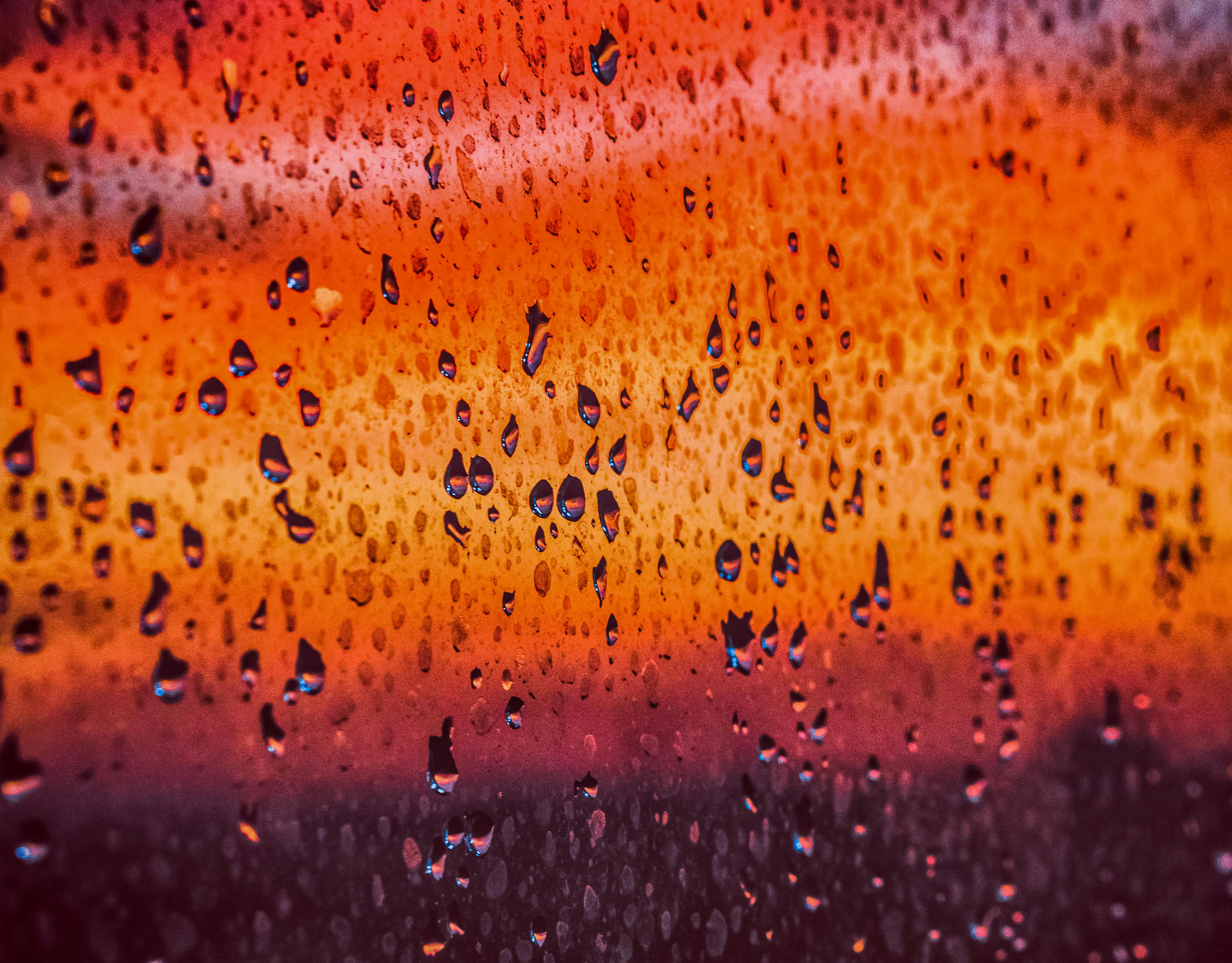 雨滴在窗户上特写，背景是生动的橙色渐变，营造出戏剧性的效果