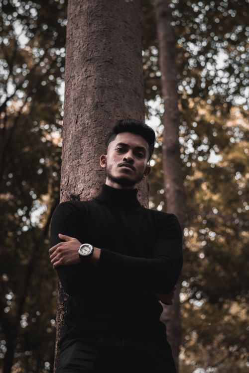 Free Portrait of a man in a black sweater leaning against a tree in a serene forest setting. Stock Photo