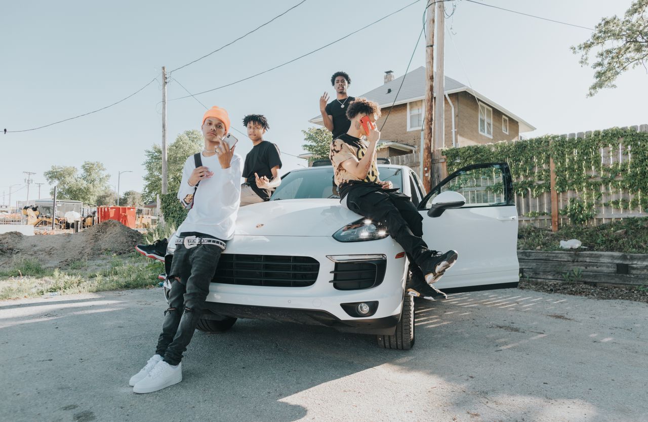 group of young men posing on and around a car in an urban neighborhood
