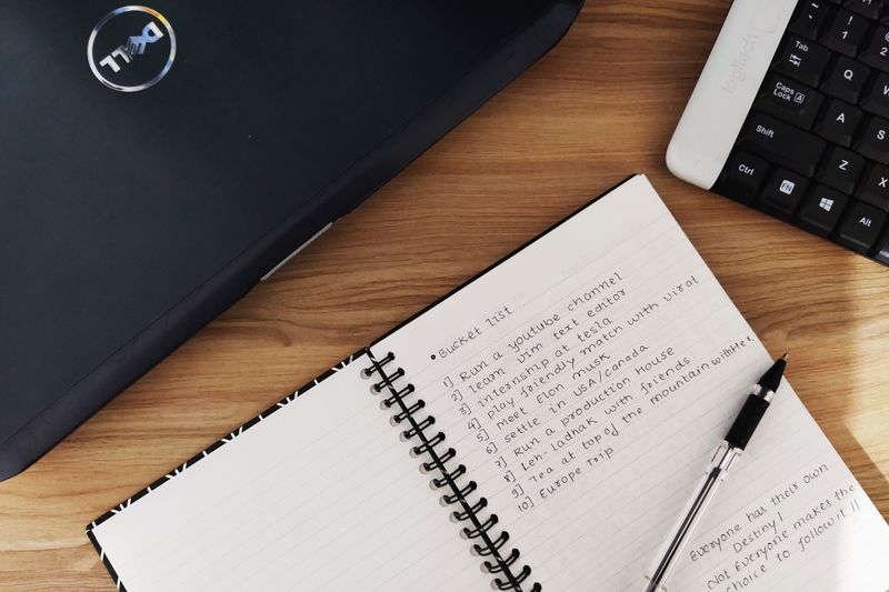 Flat lay of a workspace featuring a laptop, notebook, and keyboard on a wooden desk.