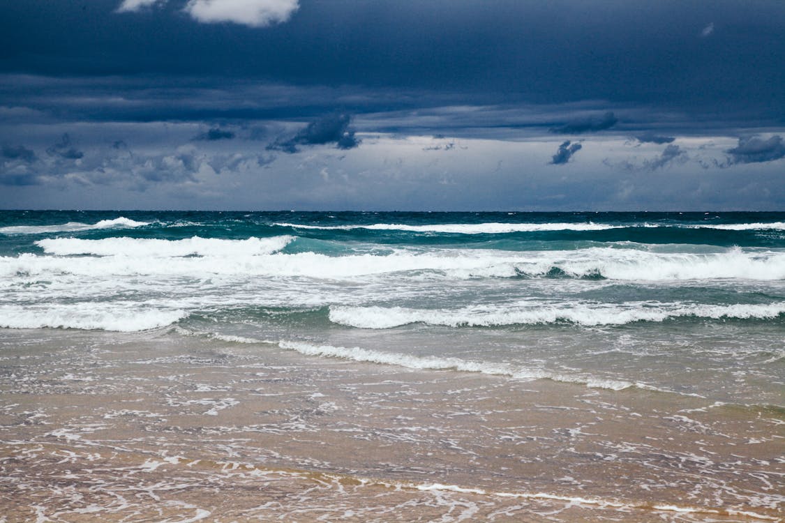Free Ocean Waves Crashing on Shore Under Dark Clouds Stock Photo