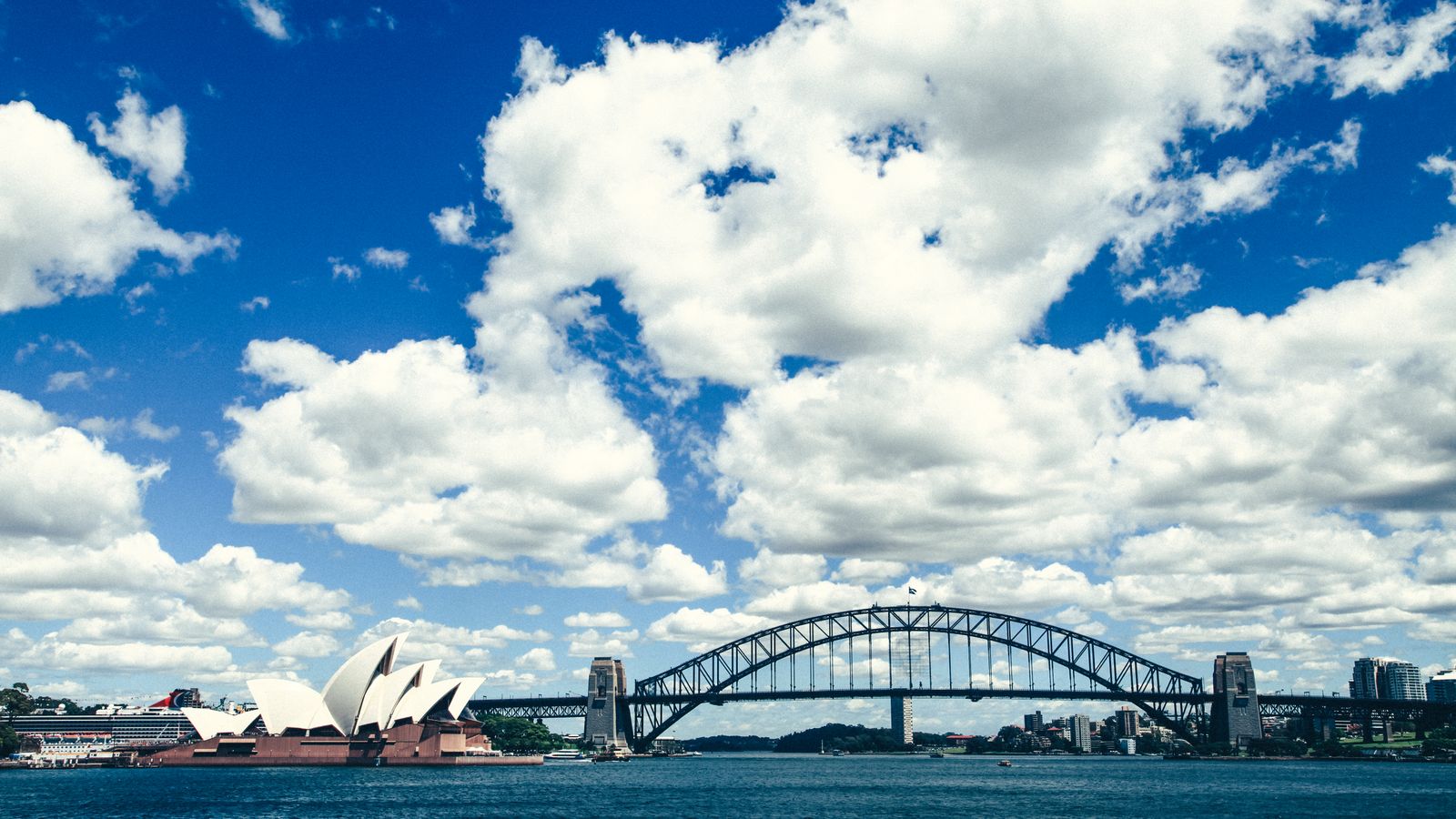 The Sydney Opera House and Harbour Bridge across the water under a blue sky.