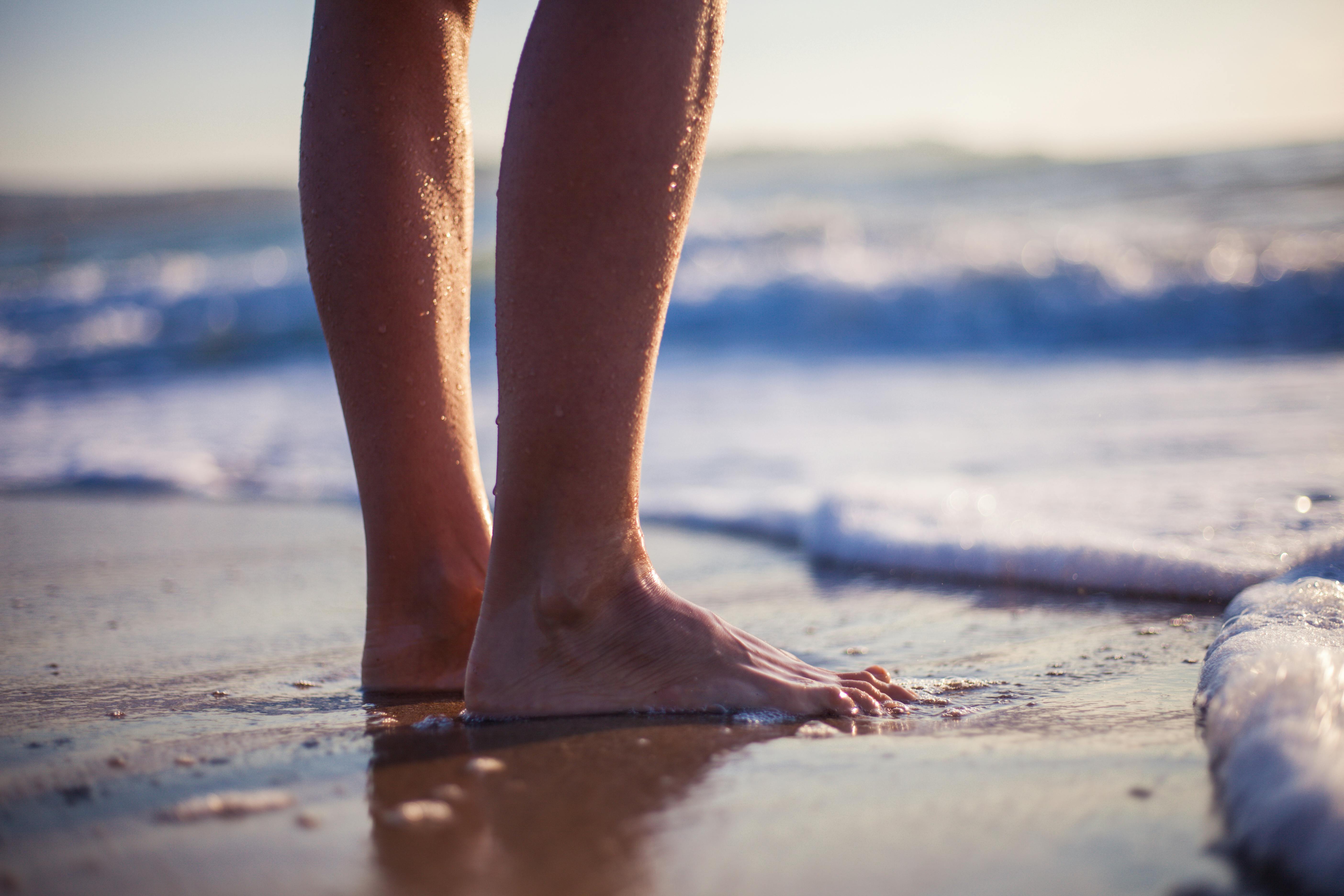 Close-up of barefoot person standing on the beach with ocean waves.