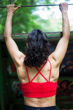 Back view of a fit woman doing a pull-up exercise in a vibrant outdoor location.