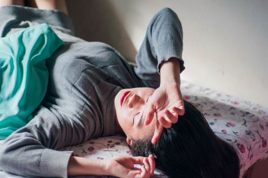 一名女子躺在室内的床上，显得放松又疲倦