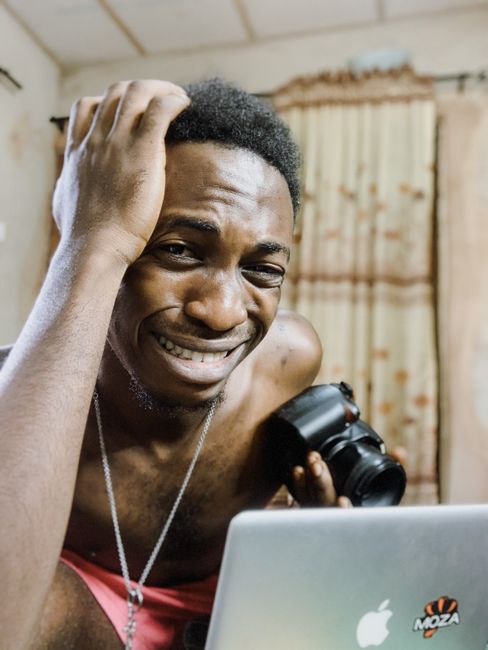 Fotomural Un joven sin camiseta parece confundido mientras sostiene una cámara DSLR y usa una laptop en el interior.