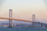 Majestic suspension bridge crossing rippling river against modern urban city on misty evening