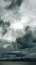 Picturesque view of dark cloudy sky with bright sunlight in center over city coastline in evening