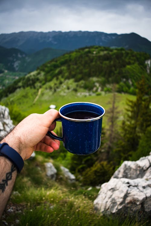 Person On A Cliff Holding Blue Mug With Black Coffee