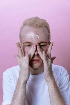 Adult male applying facial cream, focusing on skincare routine in a minimalist setting.