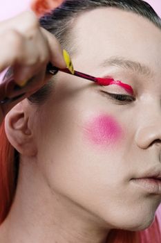 Close-up of androgynous person applying bright red eyeshadow and pink blush with artistic flair.