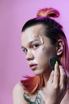 Close-up of a person applying makeup with a sponge, set against a pink background.