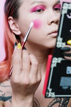 Close-up of a person applying vivid makeup, showcasing vibrant androgynous beauty style.