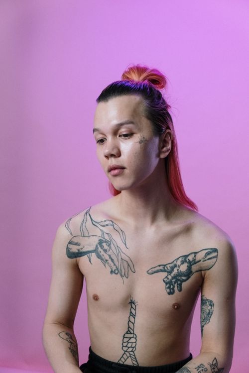 Free Stylish androgynous model posing shirtless against a vibrant pink backdrop, showcasing unique tattoos and colored hair. Stock Photo