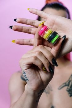 粉红色背景下，纹身手上的多元化美甲与充满活力的妆容特写