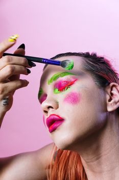 Colorful and bold artistic makeup portrait with vivid colors and creative face paint on pink background.