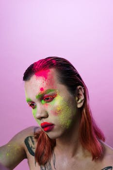 Expressive portrait of a person with vivid face paint on a pink background.