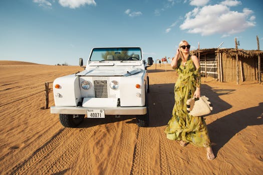 Woman poses with vintage car in a picturesque desert under clear blue sky.