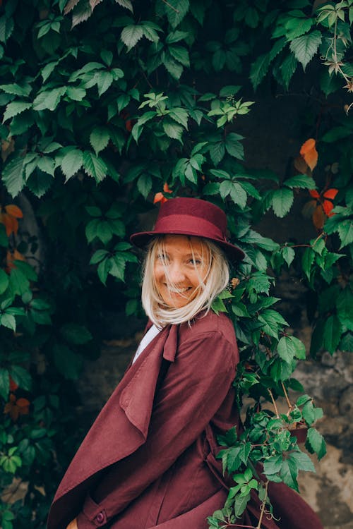 A Woman in Red Coat and Hat Standing Beside Green Plant