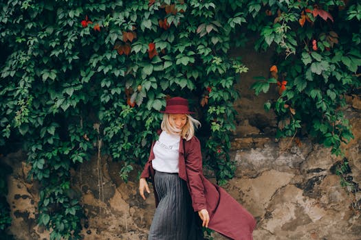 Elegant woman in burgundy coat smiling against lush ivy wall.