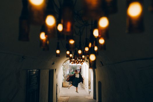 在一条狭窄、明亮的艺术走廊里，一个女人在温暖的灯光下快乐地跳跃