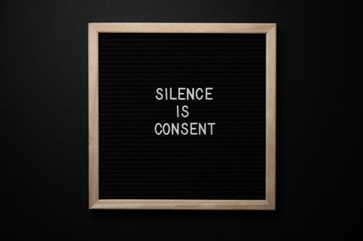 From above blackboard with written phrase SILENCE IS CONSENT on center on black background