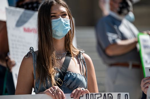 大流行期间，一名戴着口罩的年轻女子在户外抗议中举着标语