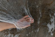 一只手在沙滩上的海水泡沫中拿着一张塑料布，突出了污染