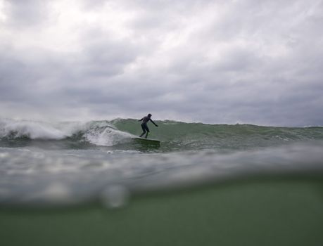 A surfer skillfully rides a wave under a cloudy sky, capturing the thrill of ocean sports.