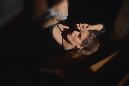 Free From above of young sensual female in black underwear touching face while lying in dark room with closed eyes Stock Photo