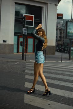 Side view of self assured young fit female in trendy outfit walking on zebra crossing in city downtown at dusk
