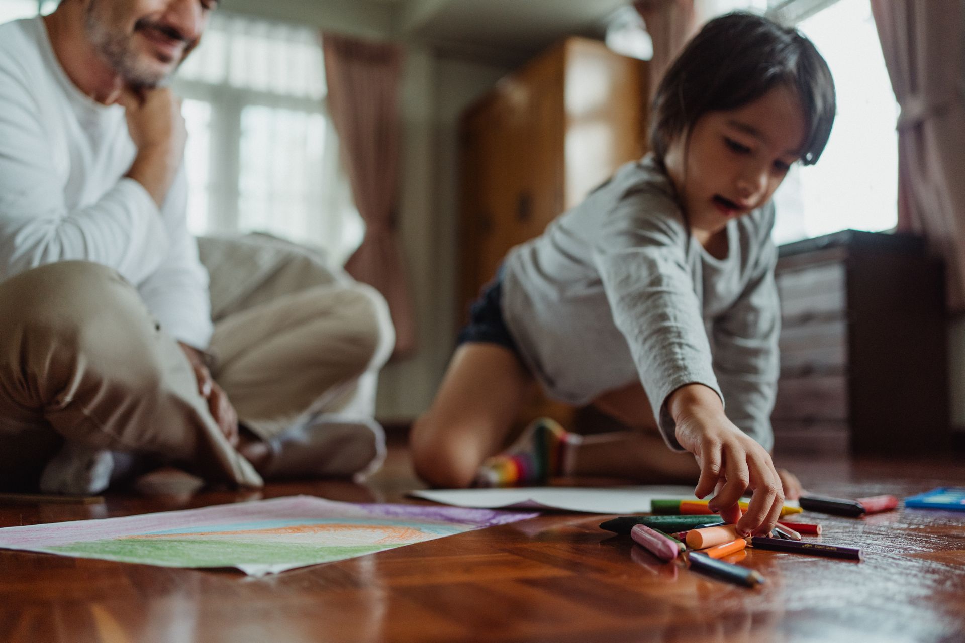 A child and adult sit on the floor engaged in a coloring activity with crayons and paper.