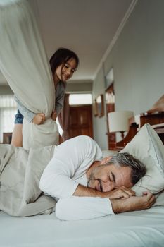 在舒适的卧室里，顽皮的父女正在玩枕头大战