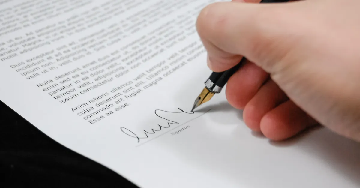 A printed agreement on a desk being signed with a pen