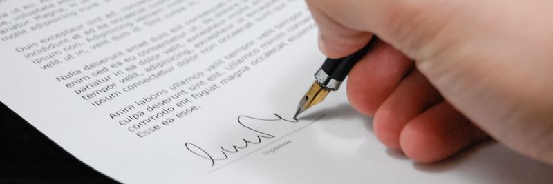 Close-up of a hand signing a legal document with a fountain pen, symbolizing signature and agreement.