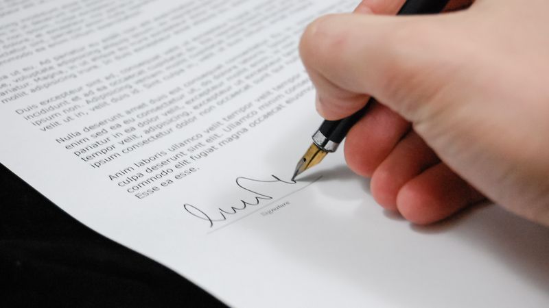 Close-up of a hand signing a legal document with a fountain pen, symbolizing signature and agreement.
