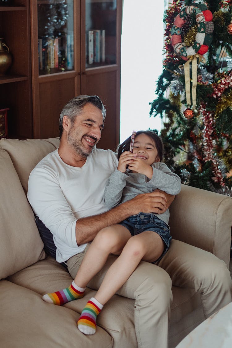 Happy Father Cuddling With Daughter On Couch