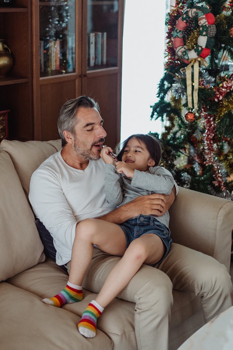 Father And Daughter Cuddling On Couch Playing