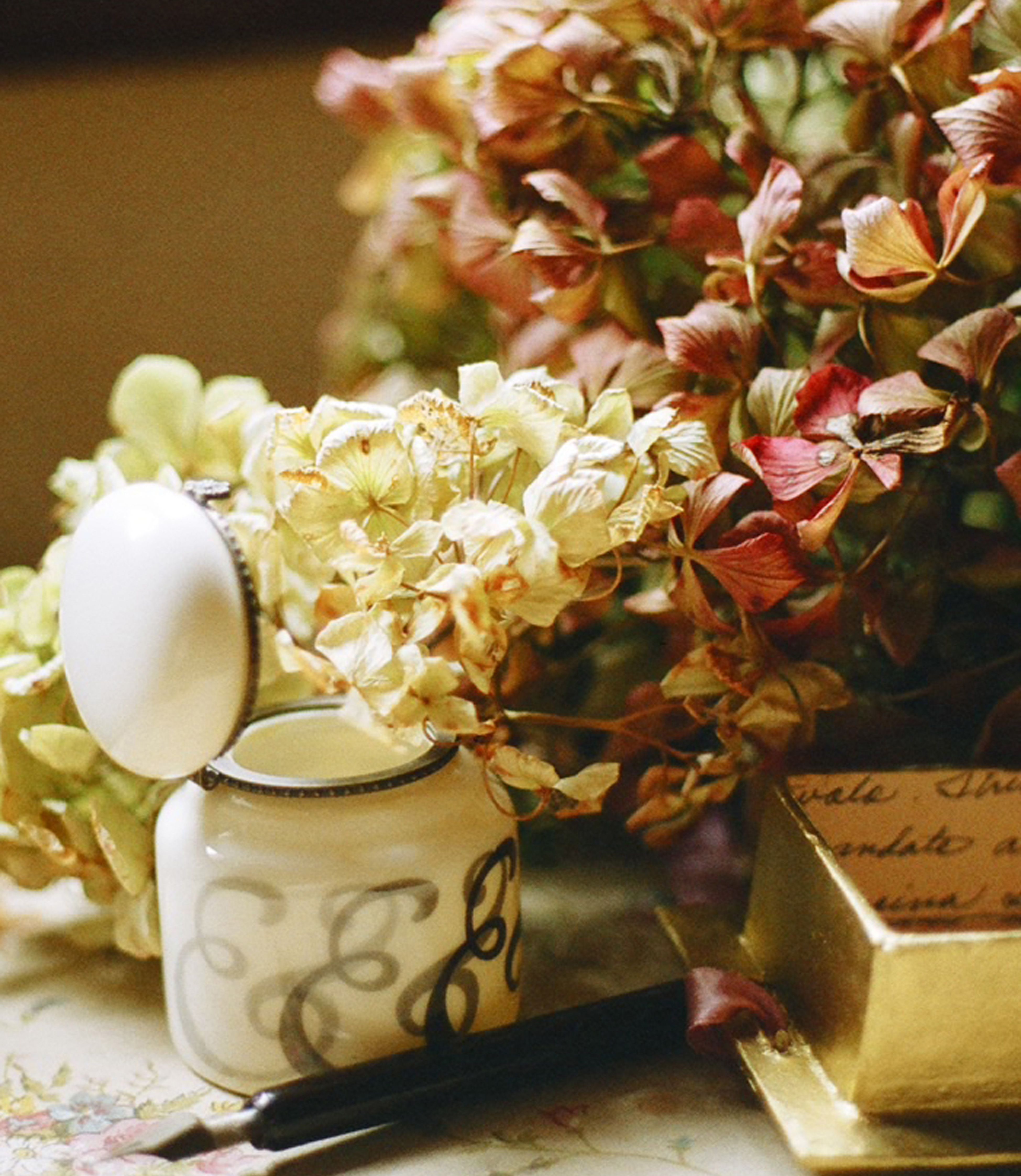 A vintage still life featuring dried flowers, an ornate jar, and a fountain pen.