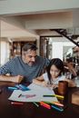 Daughter Drawing with her Father Sitting Next to her 