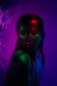霓虹艺术妆容画在潮湿的玻璃板后面，营造出生动而实验的风格